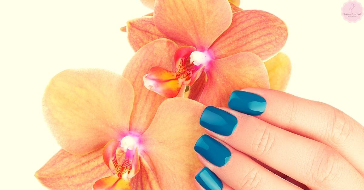 a hand holding blue Dashing Diva Glaze gel nail strips beside a close-up of an orchid flower for aesthetic contrast