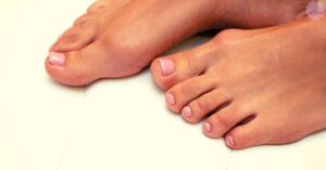 a pair of feet with neatly painted and shaped acrylic toenails, showcasing a clean pedicure.