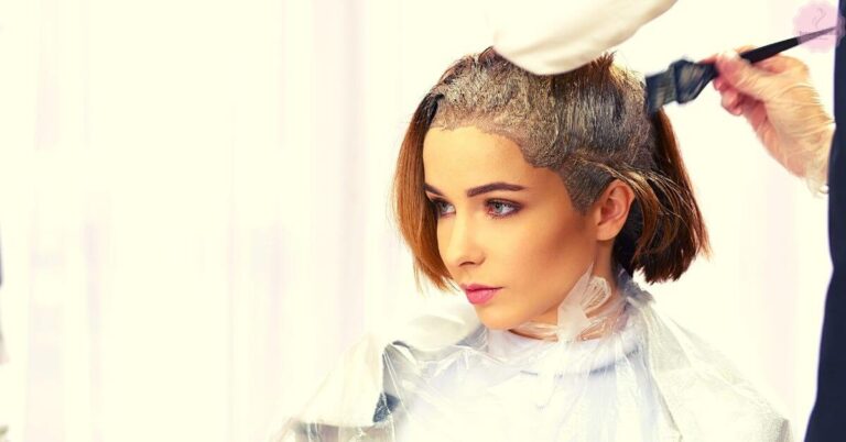 a person receiving a hair dye application with a stylist applying color to their hair under a drying cap.