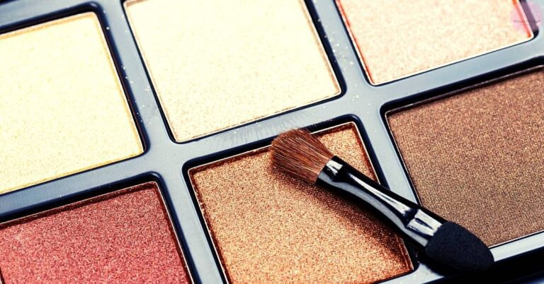 a close-up of an open eyeshadow palette with a single shimmery gold shade being applied using a fluffy brush