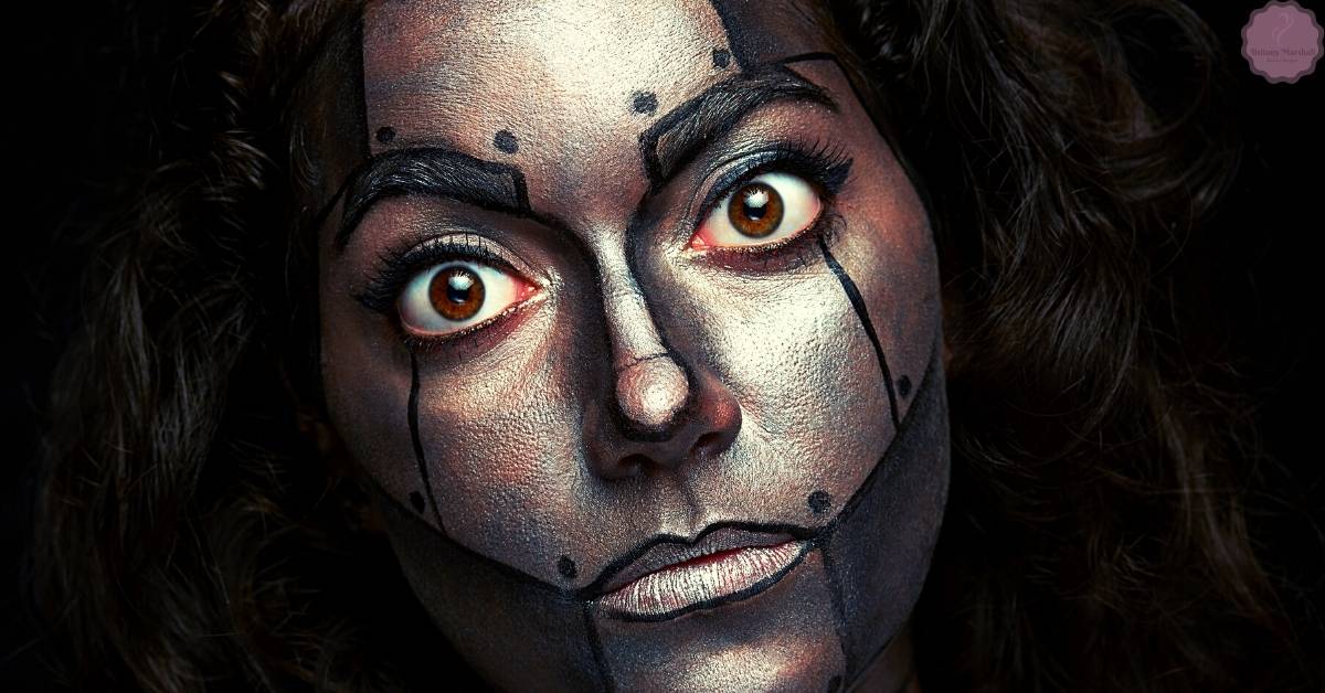 a person with dramatic face paint featuring bold, angular black lines resembling cat eye and winged eyeliner techniques to create an elongated eye effect