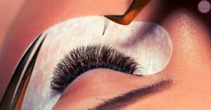 a close-up of tweezers carefully lifting an eyelash extension during the process of removing eyelash extensions at home