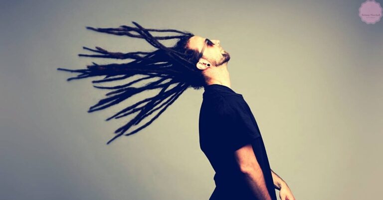 a person tilting head back with long, flowing dreadlocks lifted by wind, showcasing natural hair texture and movement.