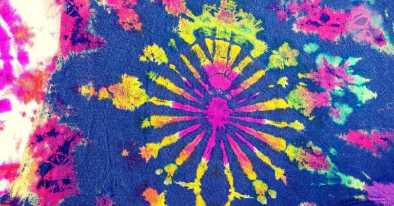 a vibrant tie dye fabric showcasing a radiant sunburst pattern with bright pink, yellow, and green hues on a dark navy background