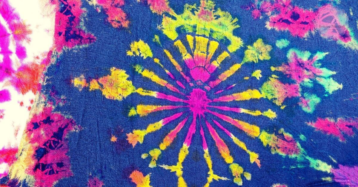 a vibrant tie dye fabric showcasing a radiant sunburst pattern with bright pink, yellow, and green hues on a dark navy background