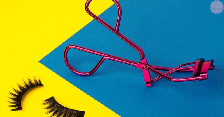a pink metal eyelash curler with false eyelashes on a vibrant blue and yellow background