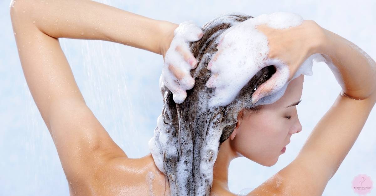 a person washing long hair with foamy shampoo under a shower stream