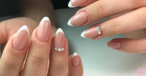 a pair of hands showcasing short, oval-shaped nails with a French manicure and decorative rhinestone accents on two nails for fat fingers.