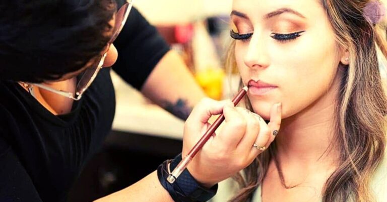 a makeup artist applying mascara to a person’s blonde eyelashes with precision using a wand