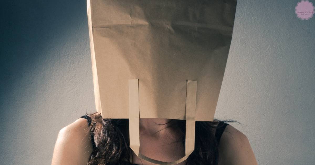 a person with their head covered by a paper bag secured with tape, obscuring their face.