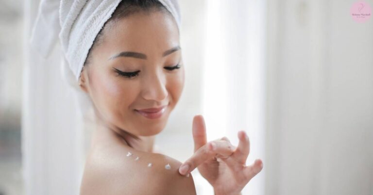 a person applying a light facial moisturizer with fingertips, wearing a towel turban, showcasing skincare routine steps.
