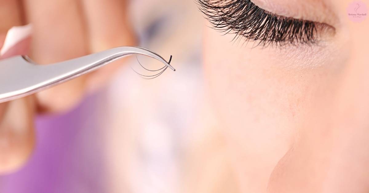 a pair of tweezers holding a single individual lash extension near a person’s natural lash line for comparison