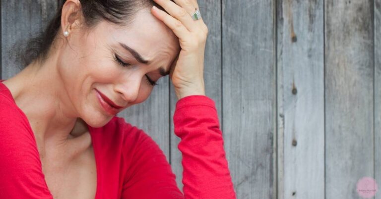 a person holding their head with a concerned expression, wearing a red top and visible earrings