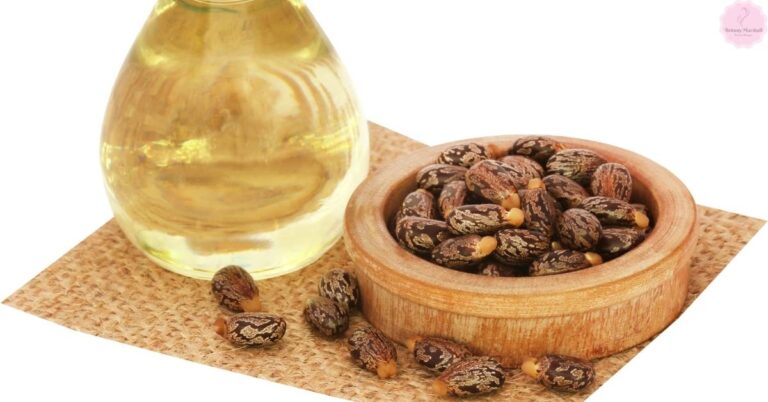 a wooden bowl filled with castor beans beside a clear glass bottle containing castor oil, on a cork surface
