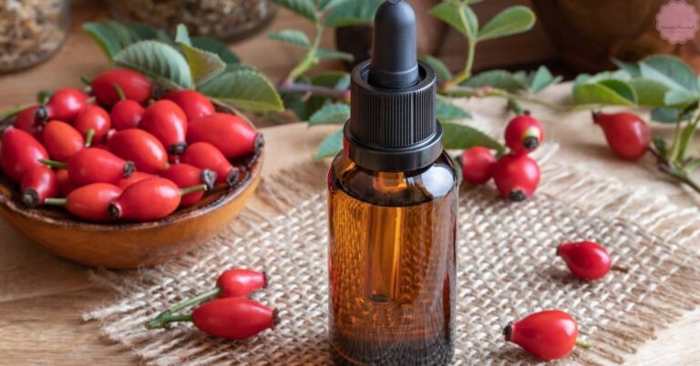 a dark glass dropper bottle of rosehip oil surrounded by fresh rosehips on a burlap cloth and wooden surface