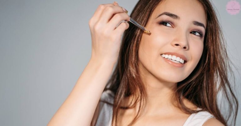 a woman smiling while applying a skincare serum near her eye area with a precision dropper.