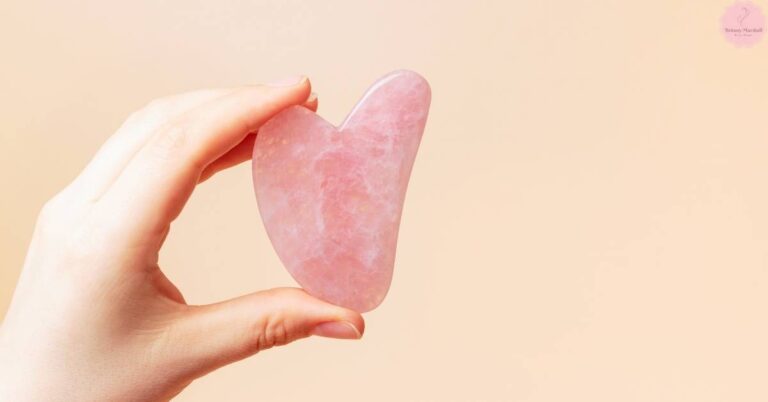 a hand holding a heart-shaped rose quartz gua sha tool for facial massage and skin care