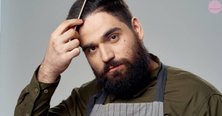a man with a beard adjusting his hair while wearing a chef’s apron, considering potential styling options like hair extensions for men.