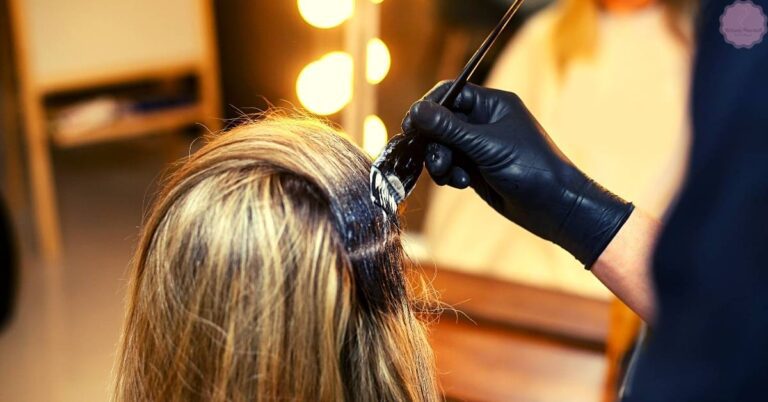 a person getting their hair dyed with a stylist applying color near the roots, wearing black gloves