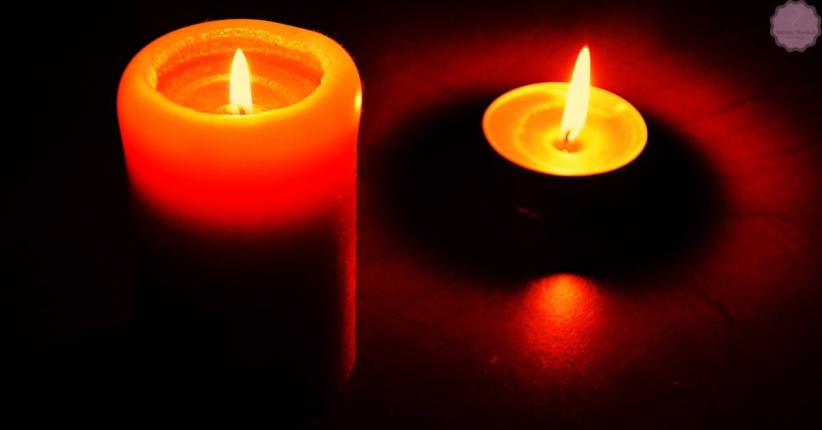 two lit candles in dark setting, showcasing a container candle and a votive candle during hardening and burn process