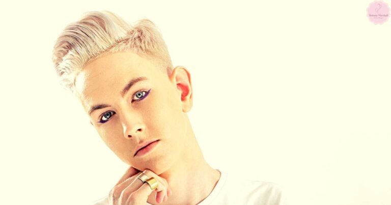 a person with bleached blonde spiked hair touching their chin, showcasing lightened hair styling