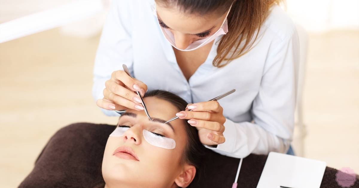 a lash technician applying eyelash extensions with precision using tweezers on a client’s closed eyes