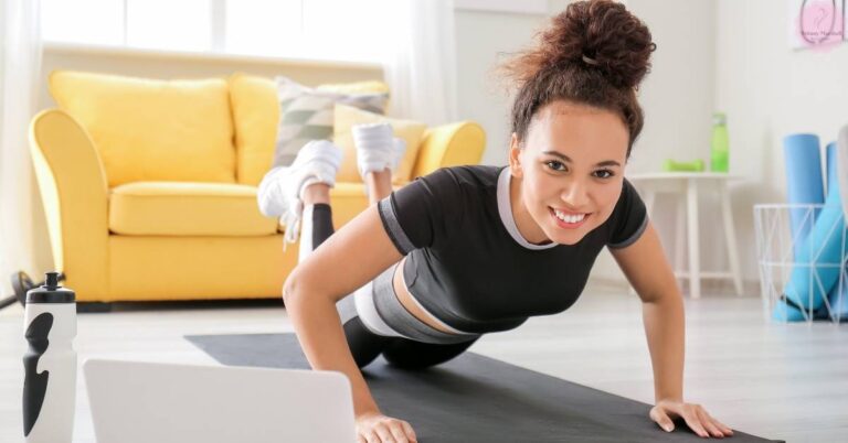 a woman performing a plank exercise on a yoga mat indoors, smiling confidently while wearing workout gloves and athletic attire.
