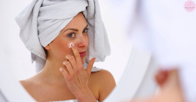 a person applying moisturizer to their face with a towel turban, focusing on skincare routine.