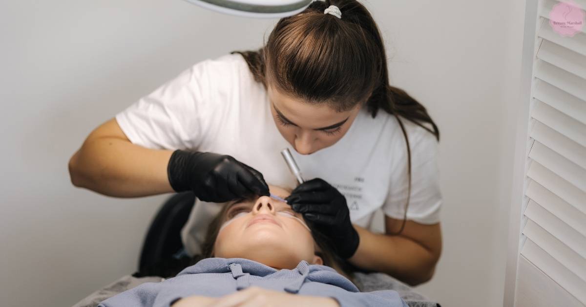 a certified lash technician in Texas applying eyelash extensions with precision on a client lying down
