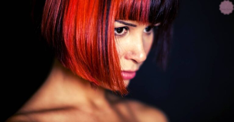 a person with short, textured bangs framing a sleek, layered hairstyle showcasing bold red highlights and subtle movement.
