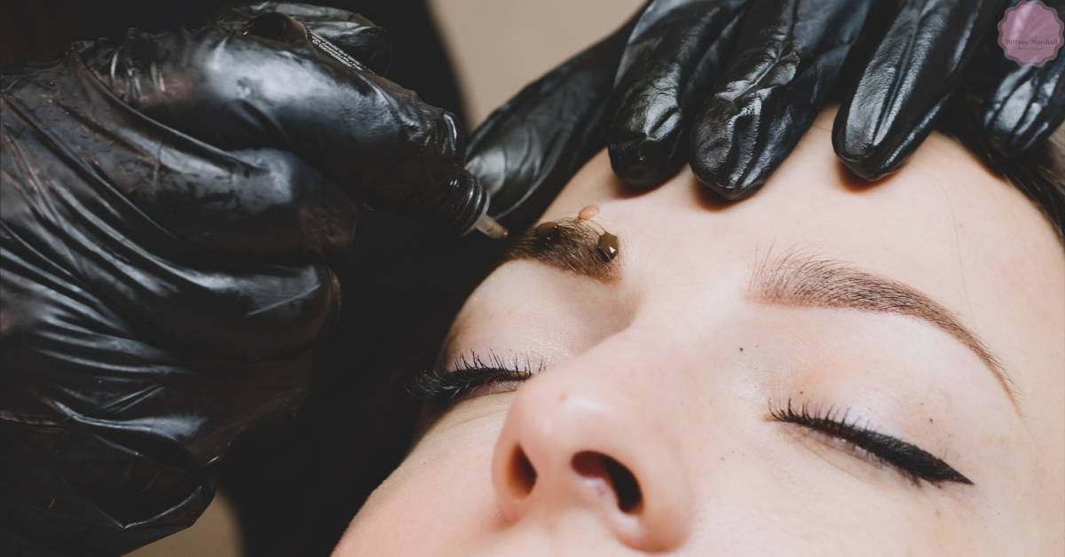 a technician performing microblading on a client’s thin eyebrows with precision using black gloves.