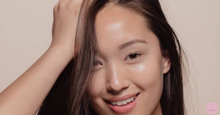 a smiling person demonstrating a natural makeup finish with skin glowed, gently touching their hair back for an Asian makeup tutorial.