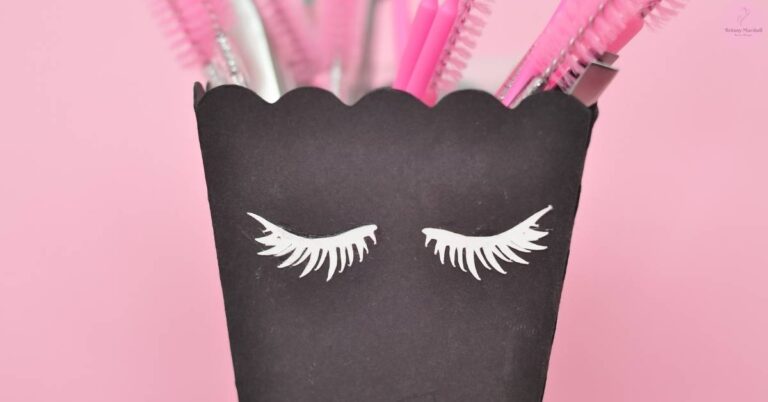 a black decorative cupcake liner with eyelash designs, holding pink feather boas