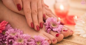 a person receiving a relaxing foot massage with hands applying gentle pressure, surrounded by delicate pink and purple flowers, showcasing a trendy pedicure with bold red nail polish.