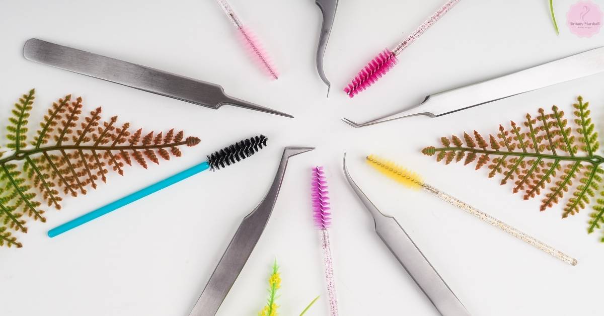a variety of eyelash extension tools and brushes arranged with decorative fern leaves for a lash room setup display