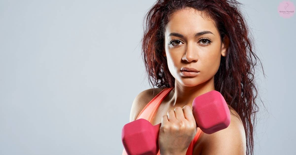 a person holding pink dumbbells, demonstrating intense exercise with visible sweat, emphasizing physical activity.