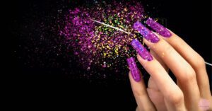 a hand displaying trendy short acrylic nails with glittery purple ombré tips against a sparkly, starry background