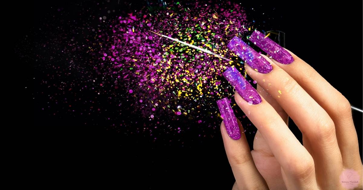 a hand displaying trendy short acrylic nails with glittery purple ombré tips against a sparkly, starry background