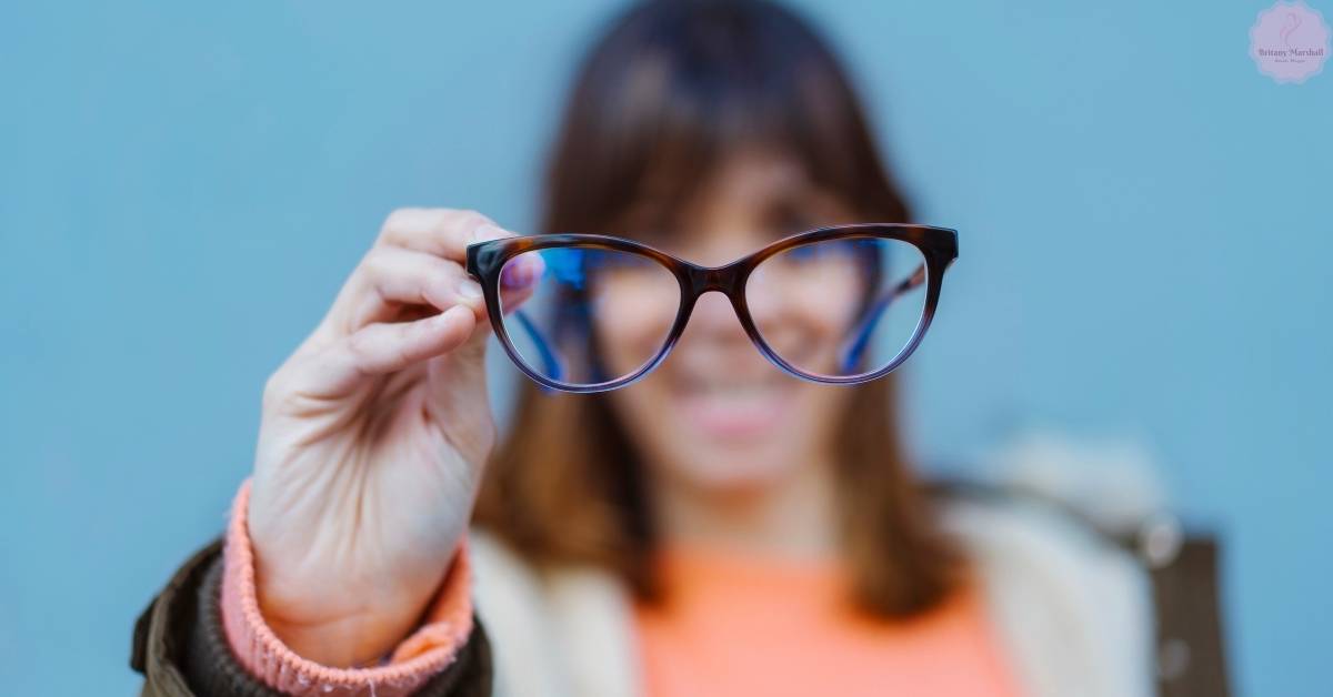 a person holding up stylish cat-eye glasses in front of their face against a blue sky background