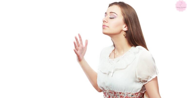 a woman with eyes closed, hand extended, appearing to enjoy a soothing floral scent.