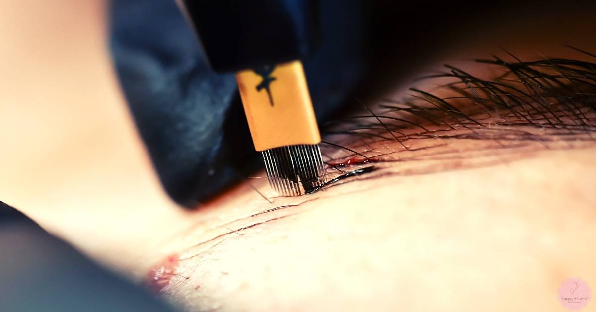 a close-up of a microblading tool creating fine strokes on skin during an eyebrow cosmetic procedure.