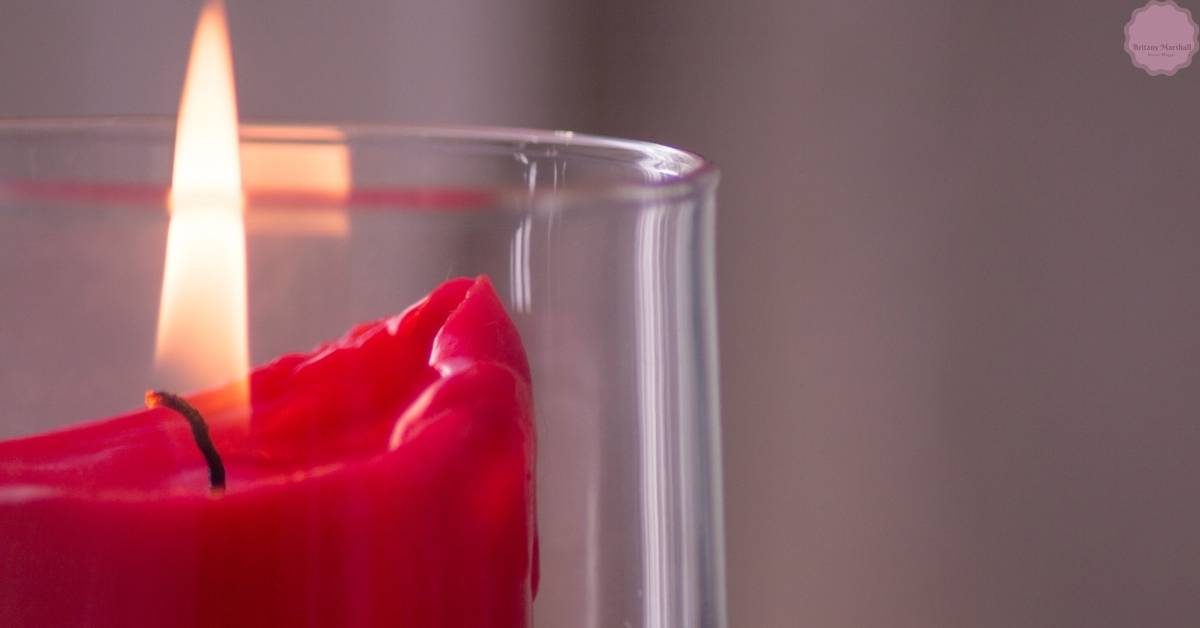 a close-up of a lit red candle with a short wick beside a glass container, illustrating potential candle flame issues