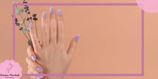 a hand holding delicate lavender flowers with soft periwinkle and mauve nail polish on pale skin