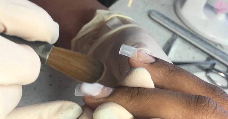 a hand applying clear acrylic powder to nails using a wooden stick for DIY nail enhancement