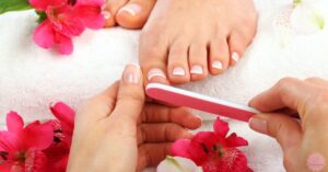 a professional giving a deluxe pedicure, carefully filing toenails with a nail file surrounded by decorative flowers.