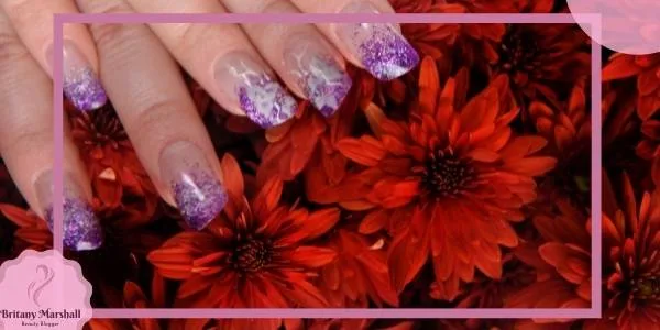 a hand showcasing light mauve and lavender glitter nail polish against vibrant red flowers