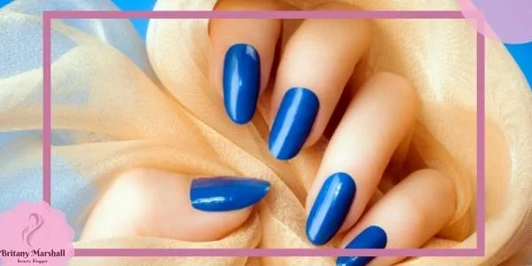 a hand with bright periwinkle blue nail polish on almond-shaped nails against a soft fabric backdrop