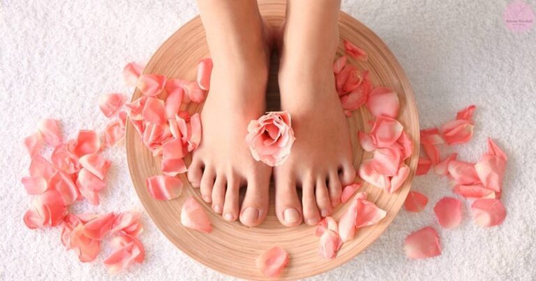 a wooden pedicure basin filled with pink rose petals holding feet soaking in a foot beauty treatment