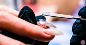 a hand using a metal file and cuticle pusher to carefully remove polygel nail buildup from a natural nail