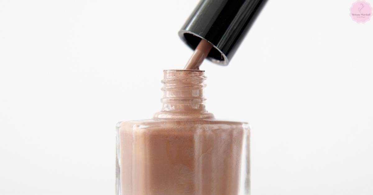 a close-up of a light brown nail polish bottle with a dropper brush dispensing a mocha-toned acrylic nail polish